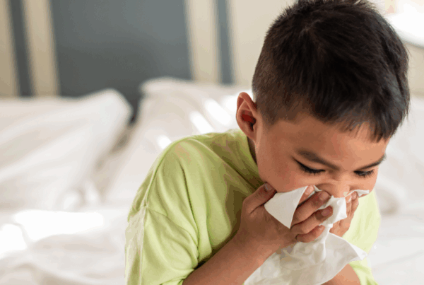 Child blowing nose while sitting on bed, showing symptoms of sinusitis in children.